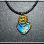 Pendentif en fil de cuivre doré enroulé autour d'un cabochon de verre avec motif floral.