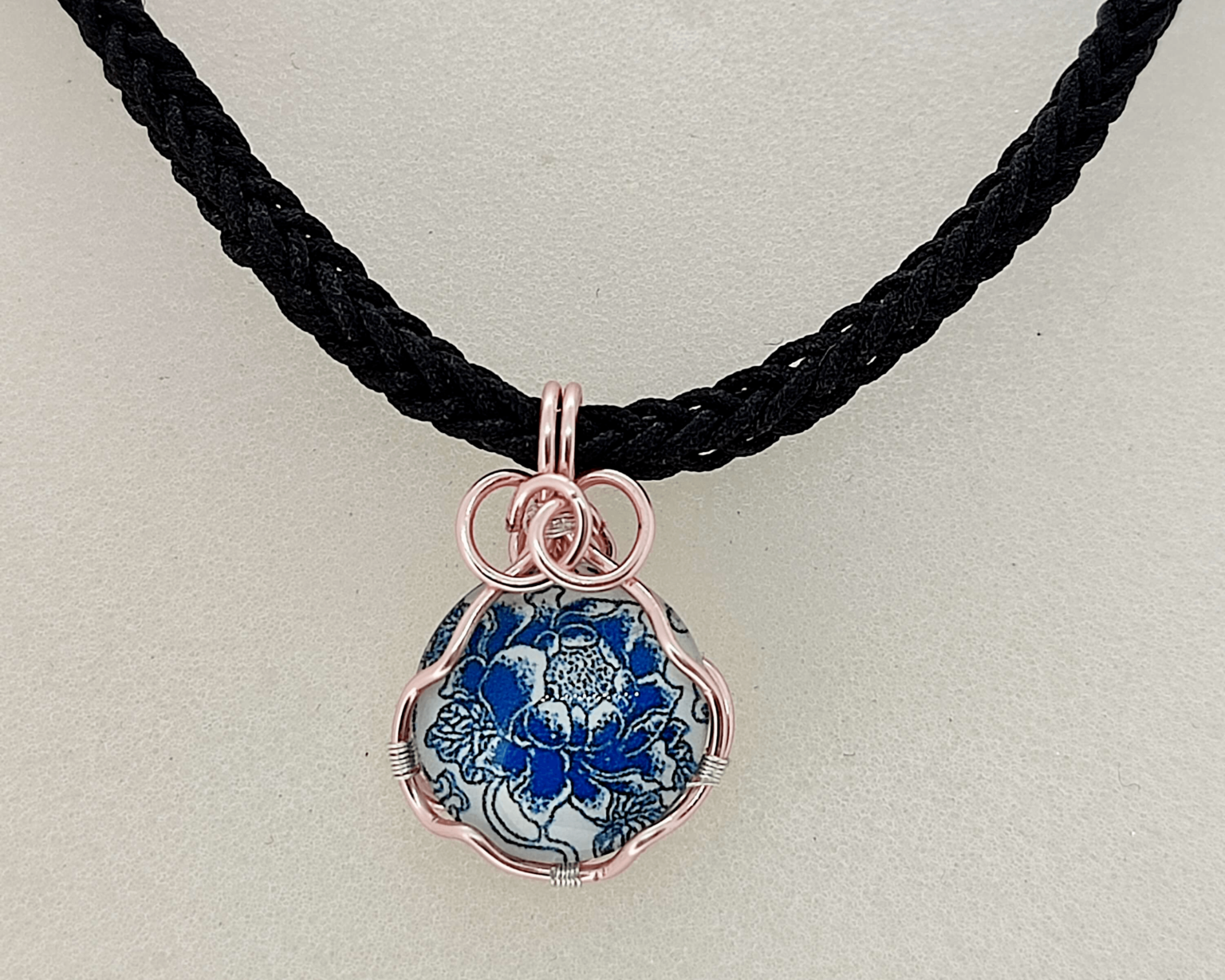 Pendentif en fil de cuivre doré enroulé autour d'un cabochon de verre avec motif floral.