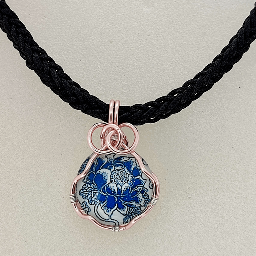 Pendentif en fil de cuivre doré enroulé autour d'un cabochon de verre avec motif floral.